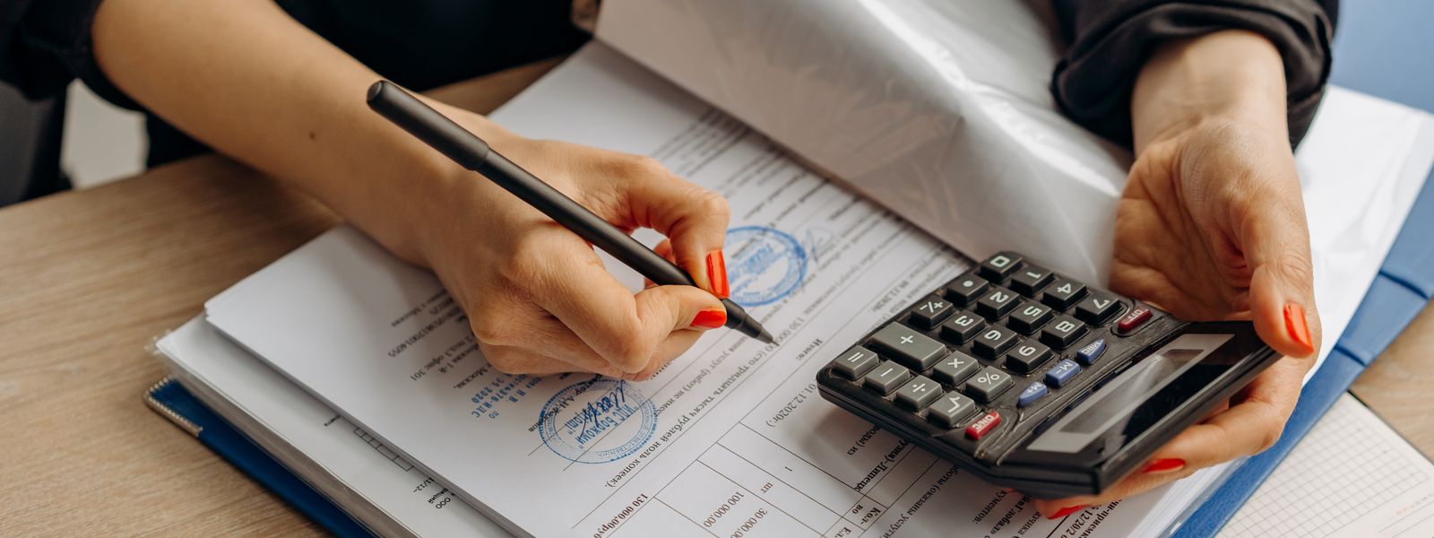 An accountant using a calculator and signing paperwork, showcasing financial analysis.