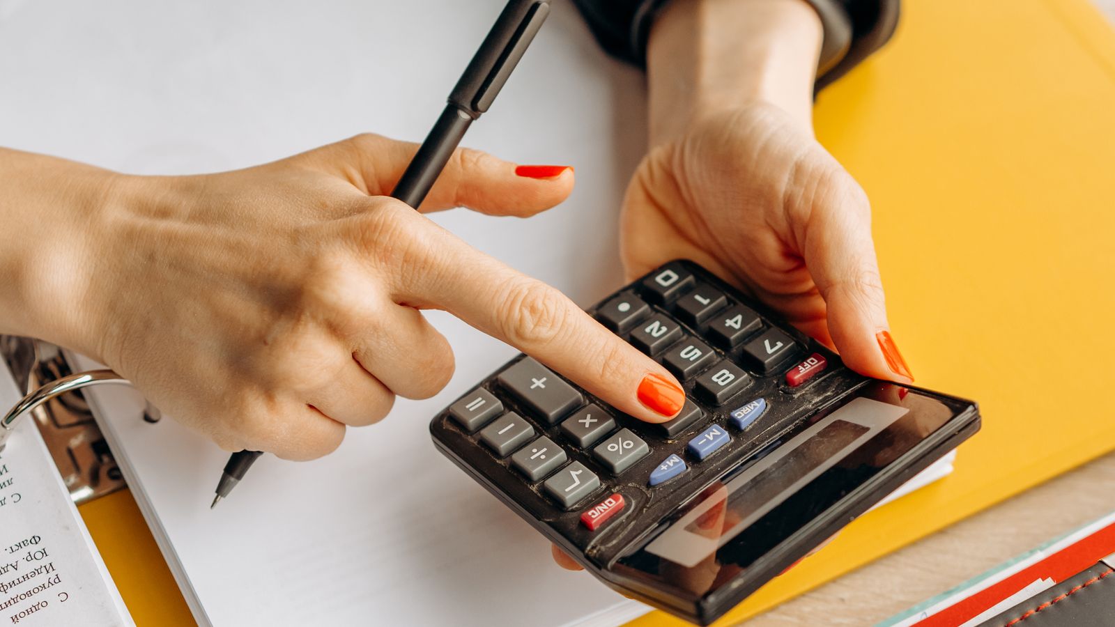 A person using a calculator beside paperwork and an open folder.