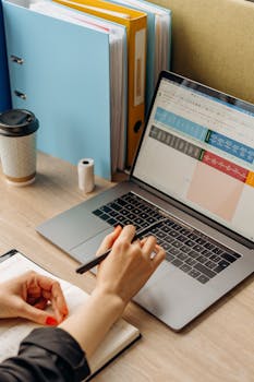 A person working on a laptop with documents and coffee in a modern workspace.