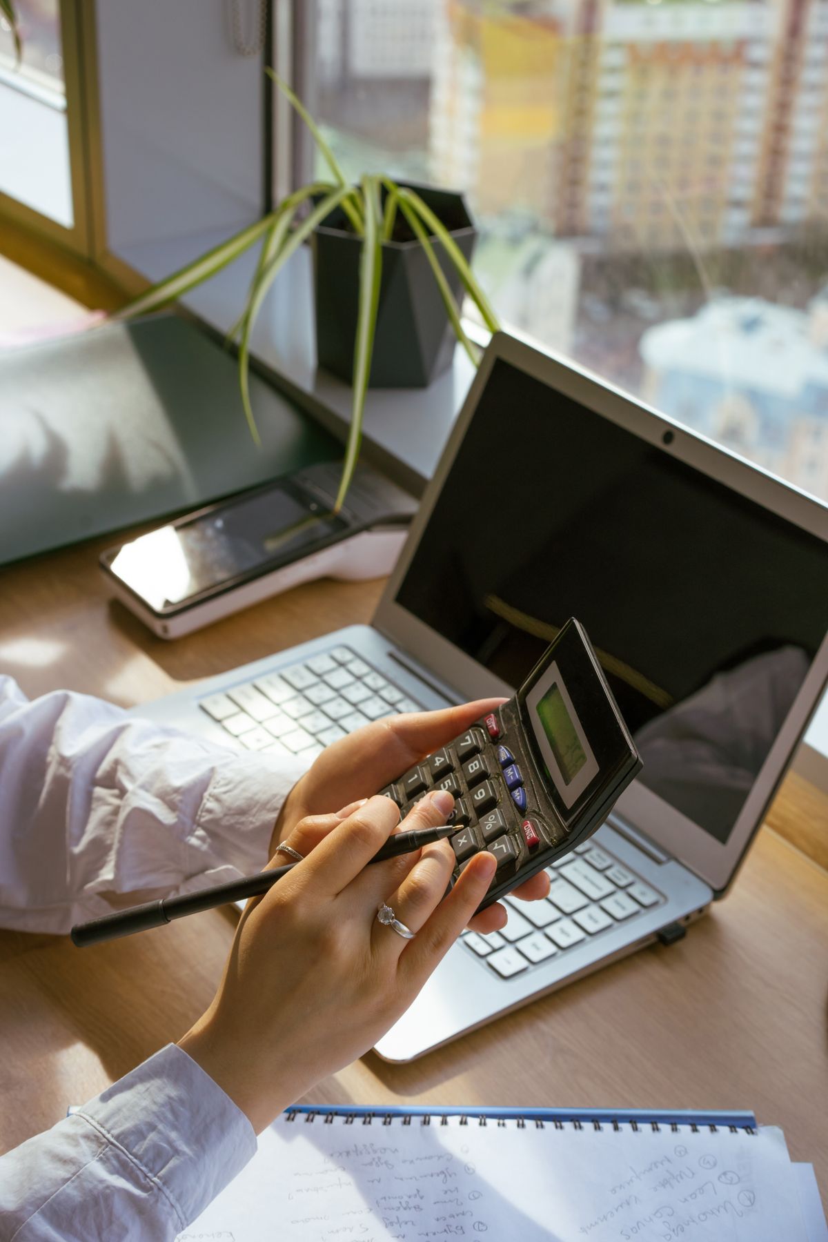 Professional using a calculator and laptop for billing and accounts