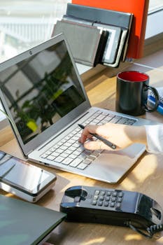 A modern office desk setup featuring a laptop, smartphone, and landline phone, focused on productivity.