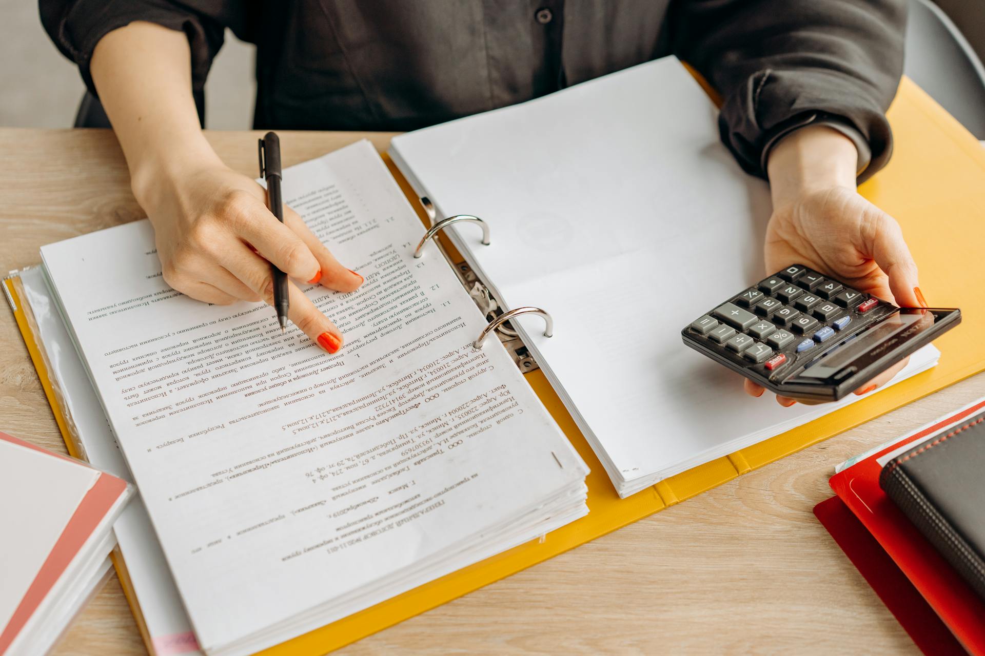 A woman reviewing documents and using a calculator on a wooden table.