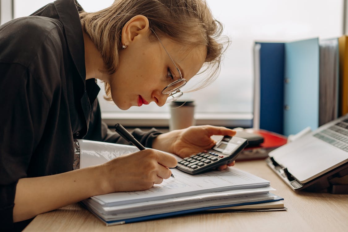 Free A Woman Writing on a Book while Holding a Calculator Stock Photo