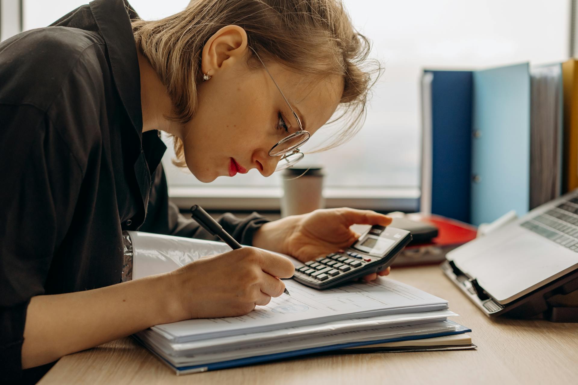 Young woman diligently working on accounting with a calculator and documents. Perfect for business and finance themes.