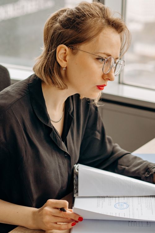 Free Serious woman with eyeglasses working on paperwork in an office setting. Stock Photo