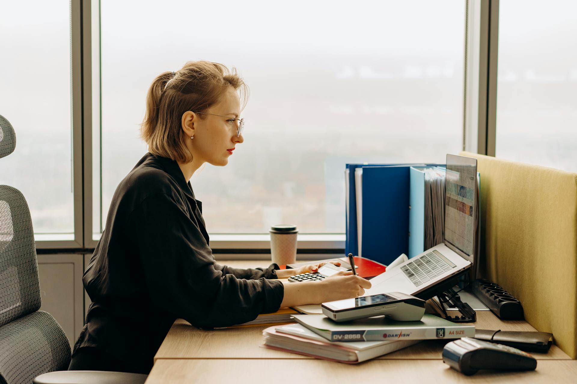 Dedicated woman using laptop and calculator in modern office setting.