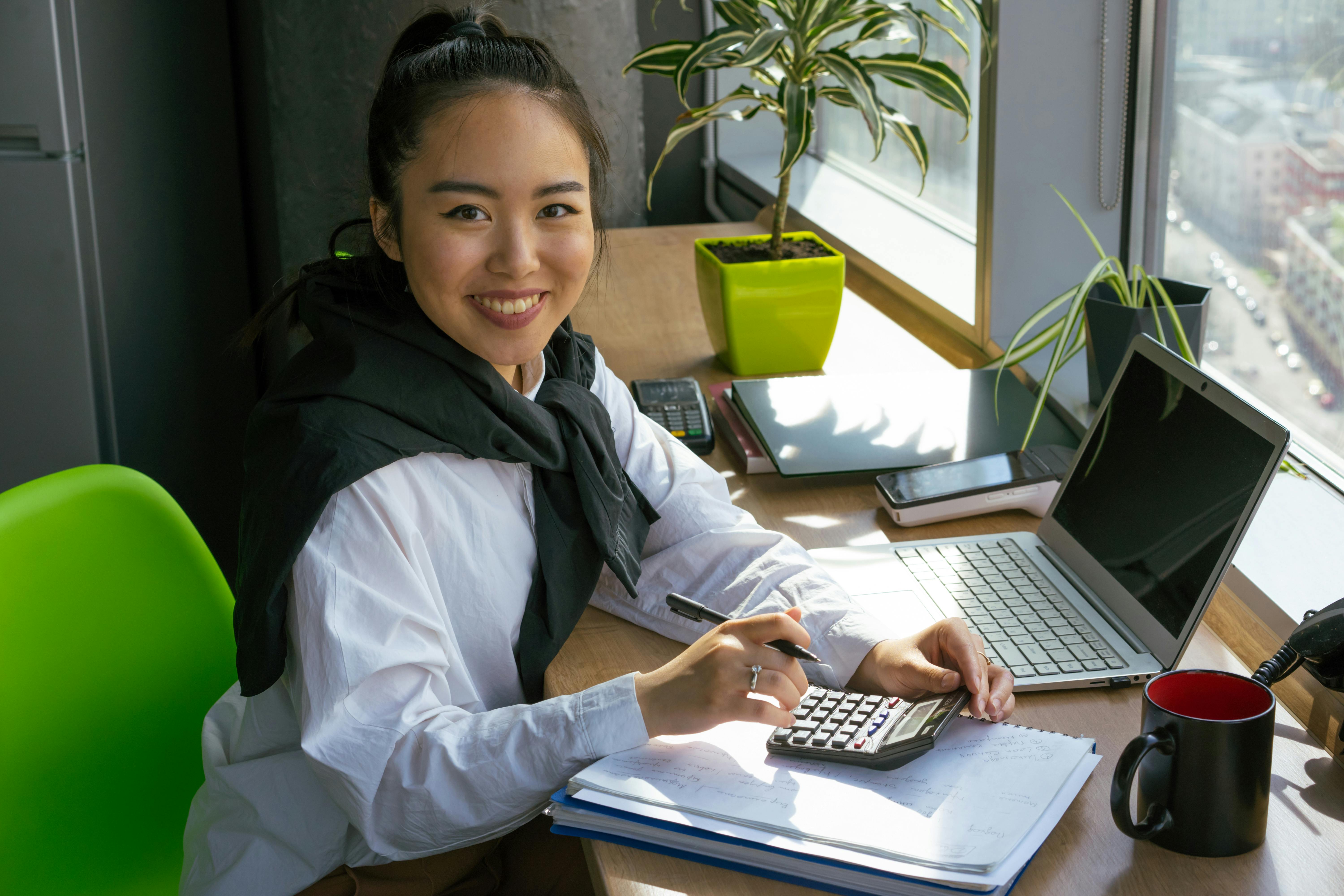 woman in white dress shirt using calculator near office window