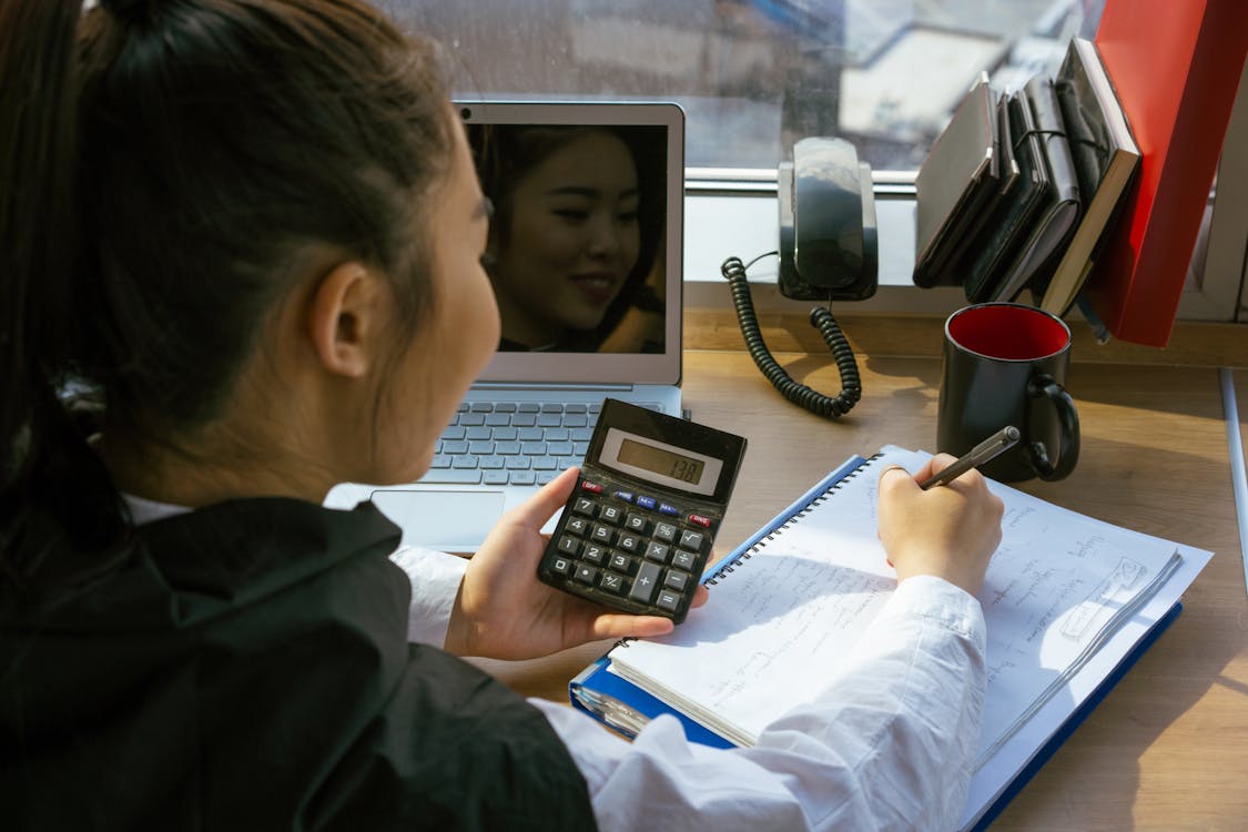 Woman Writing on a Notepad while Holding a Calculator