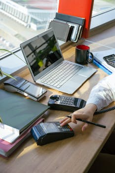 A high-angle view of a workspace with electronic devices and payment terminal on a desk.