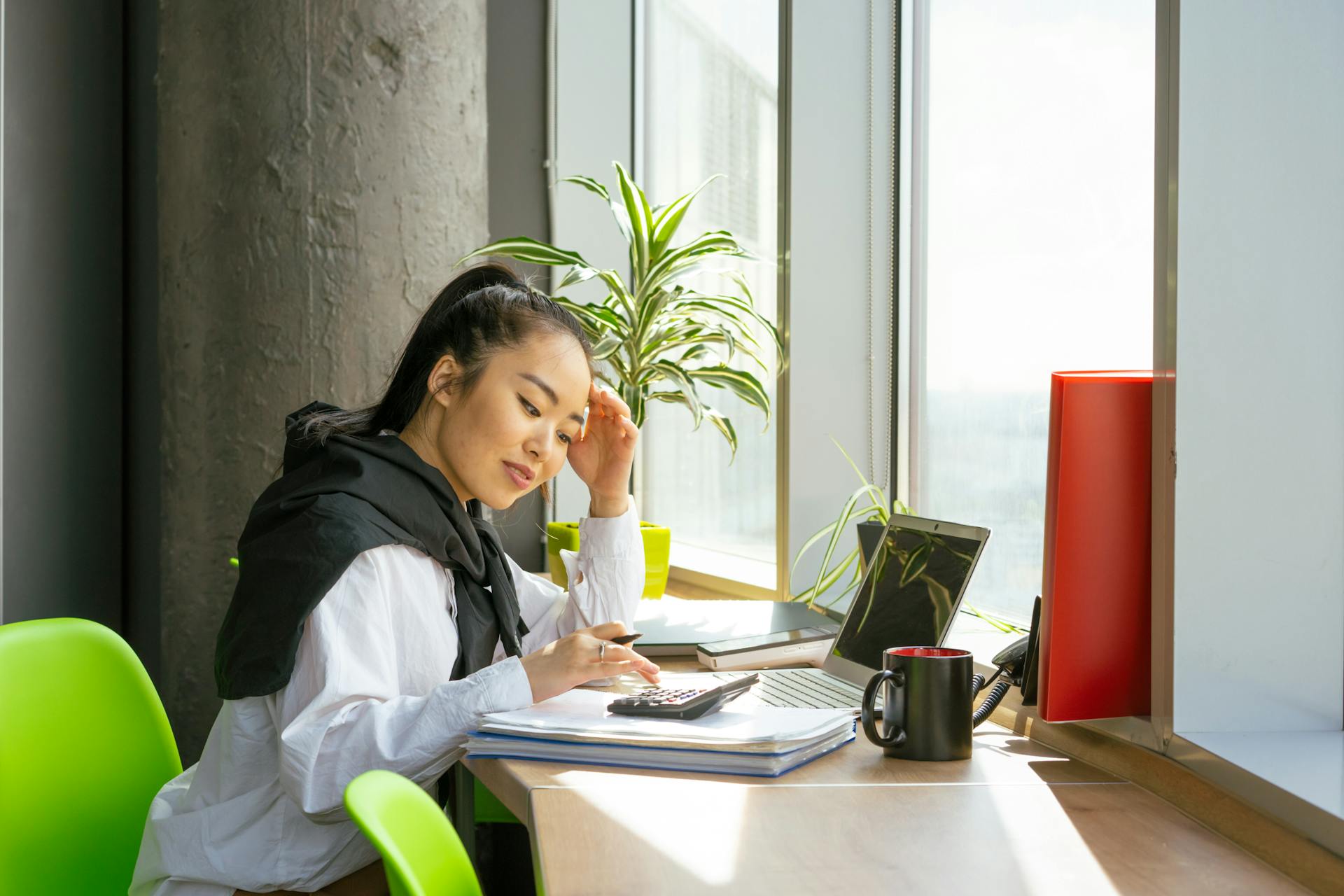 Asian woman working on finances with a calculator in a bright modern office.