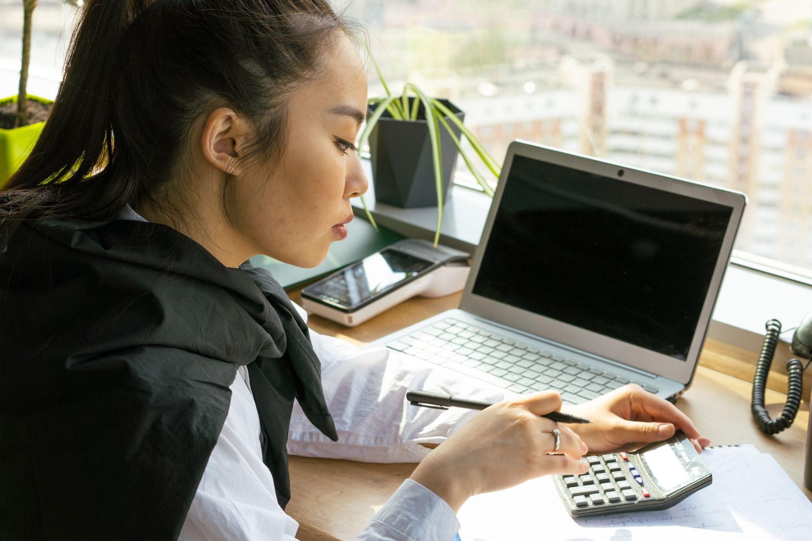Asian woman using a calculator and laptop while reviewing personal finances
