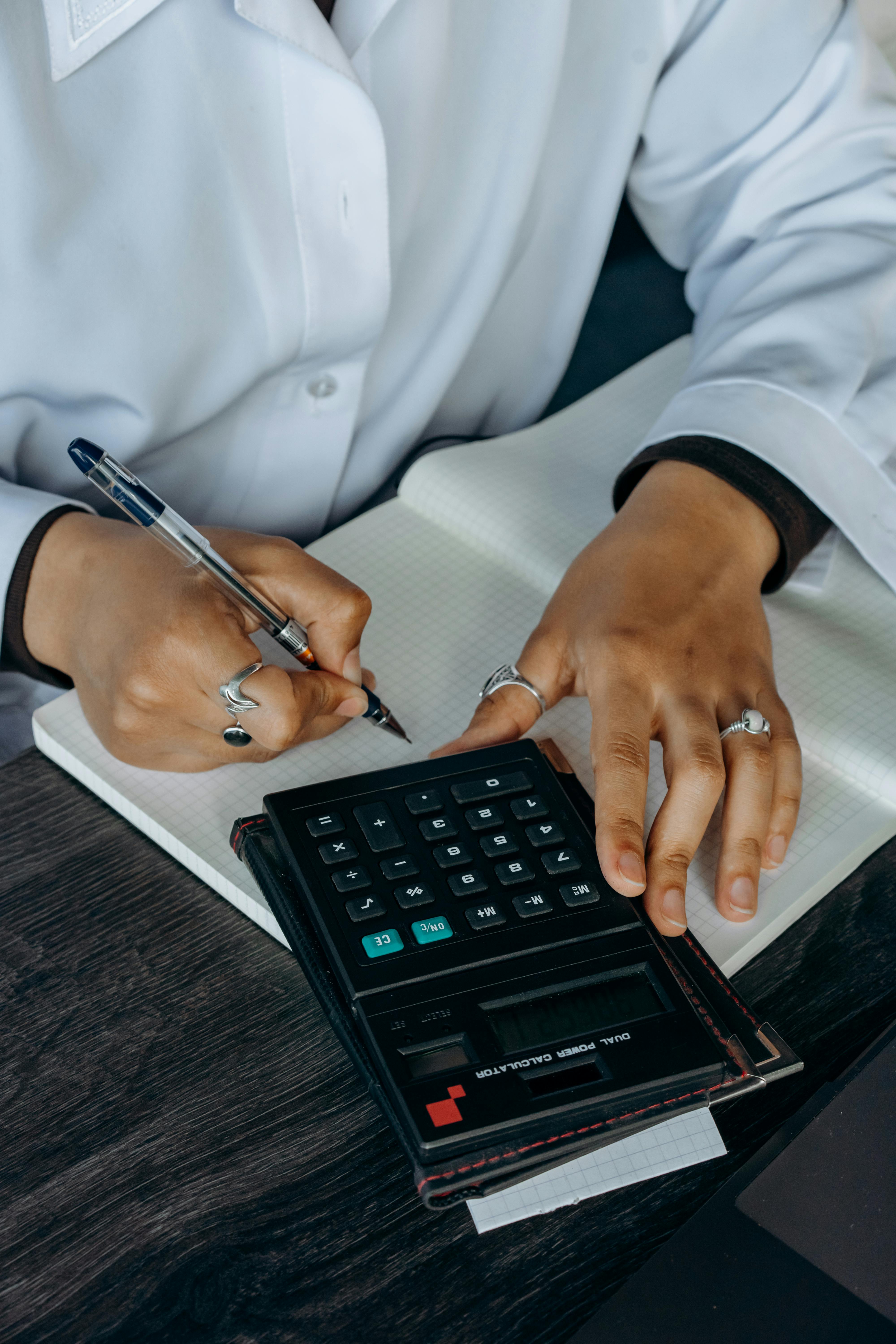 person in white dress shirt holding black pen and black calculator