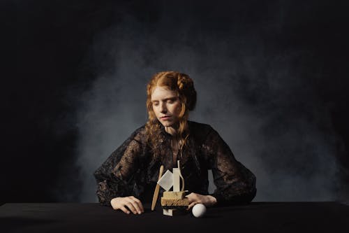 Young Girl Sitting on Black Long Sleeve Blouse in Front of Bath Essentials Display on a Table