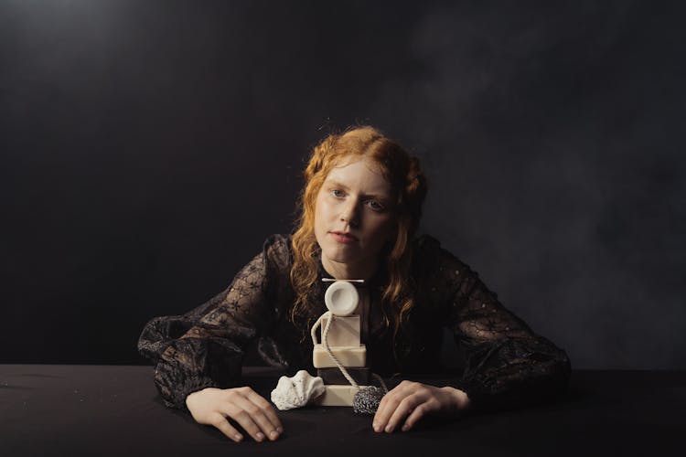 Young Girl Sitting On Black Long Sleeve Blouse In Front Of Bath Essentials Display On A Table