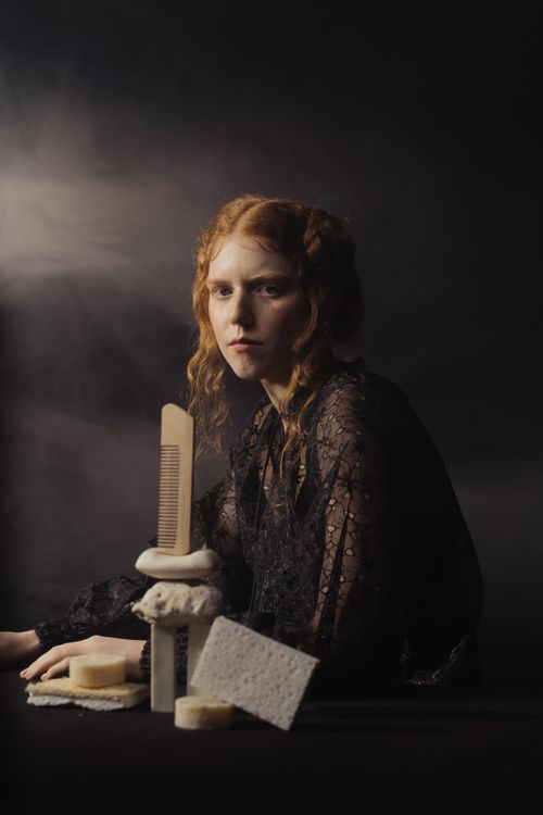 Free A young woman in dark attire seated with bath essentials in a moody, artistic setting. Stock Photo