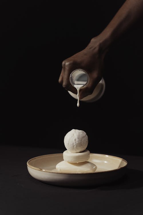 Person Pouring Liquid Soap on Soap Bars on a Ceramic Plate