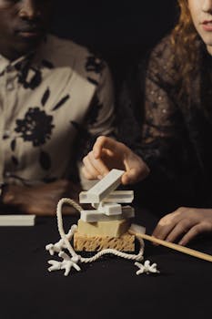 A close-up of hands playing with soap blocks, rope and coral on a dark table.