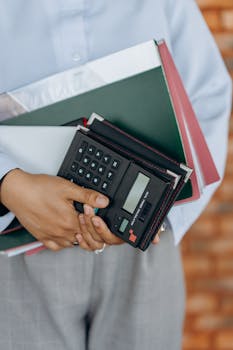 Close-up of a person holding a calculator and folders, symbolizing office work and organization.