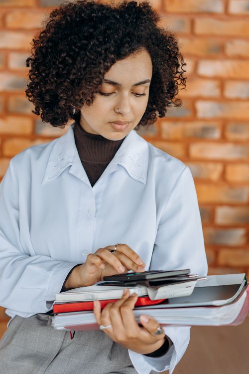 Free Young woman using calculator with paperwork indoors, focusing on financial tasks in a modern office setting. Stock Photo