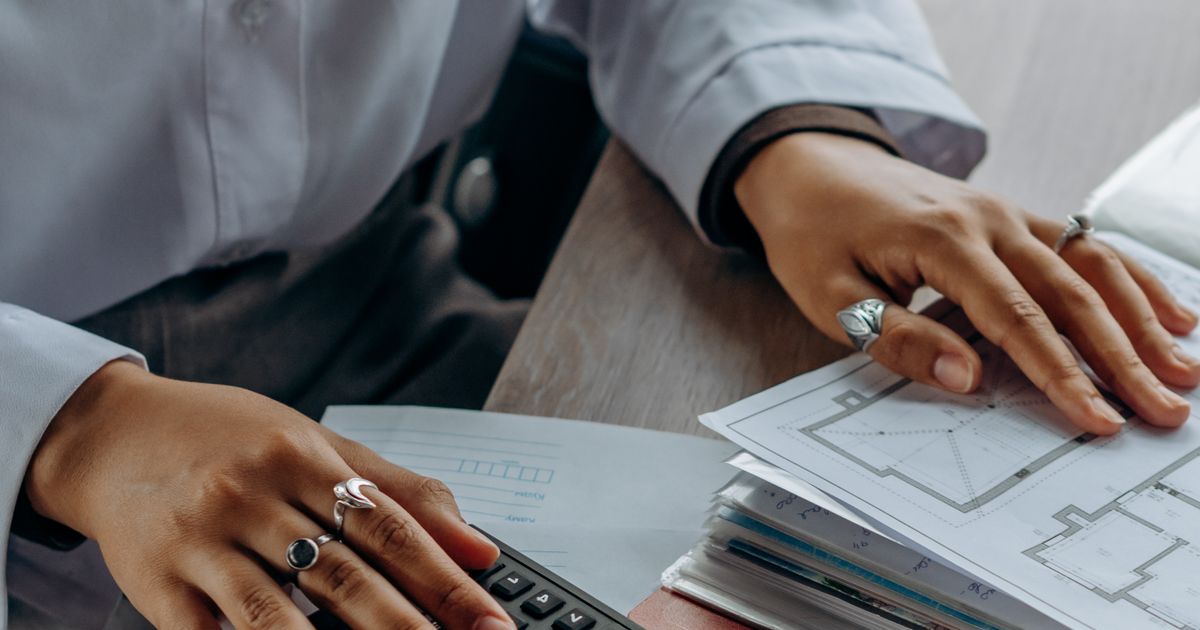 A person reviewing financial documents and using a calculator at a desk.