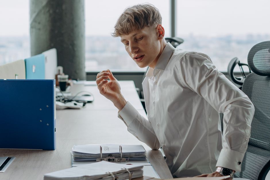 Worker experiencing injury at desk with concerned colleague nearby providing support