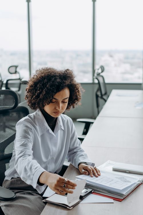 Free Woman with curly hair organizing documents at office desk, showcasing a professional work environment. Stock Photo