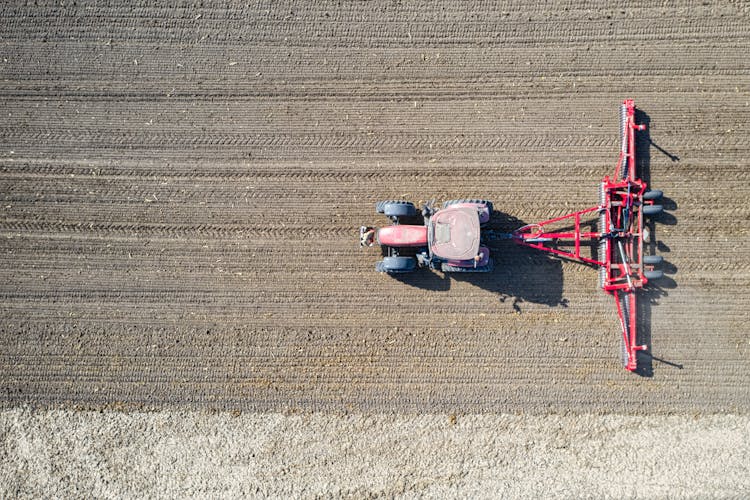 Top View Shot Of Red Tractor Plowing The Farm Field