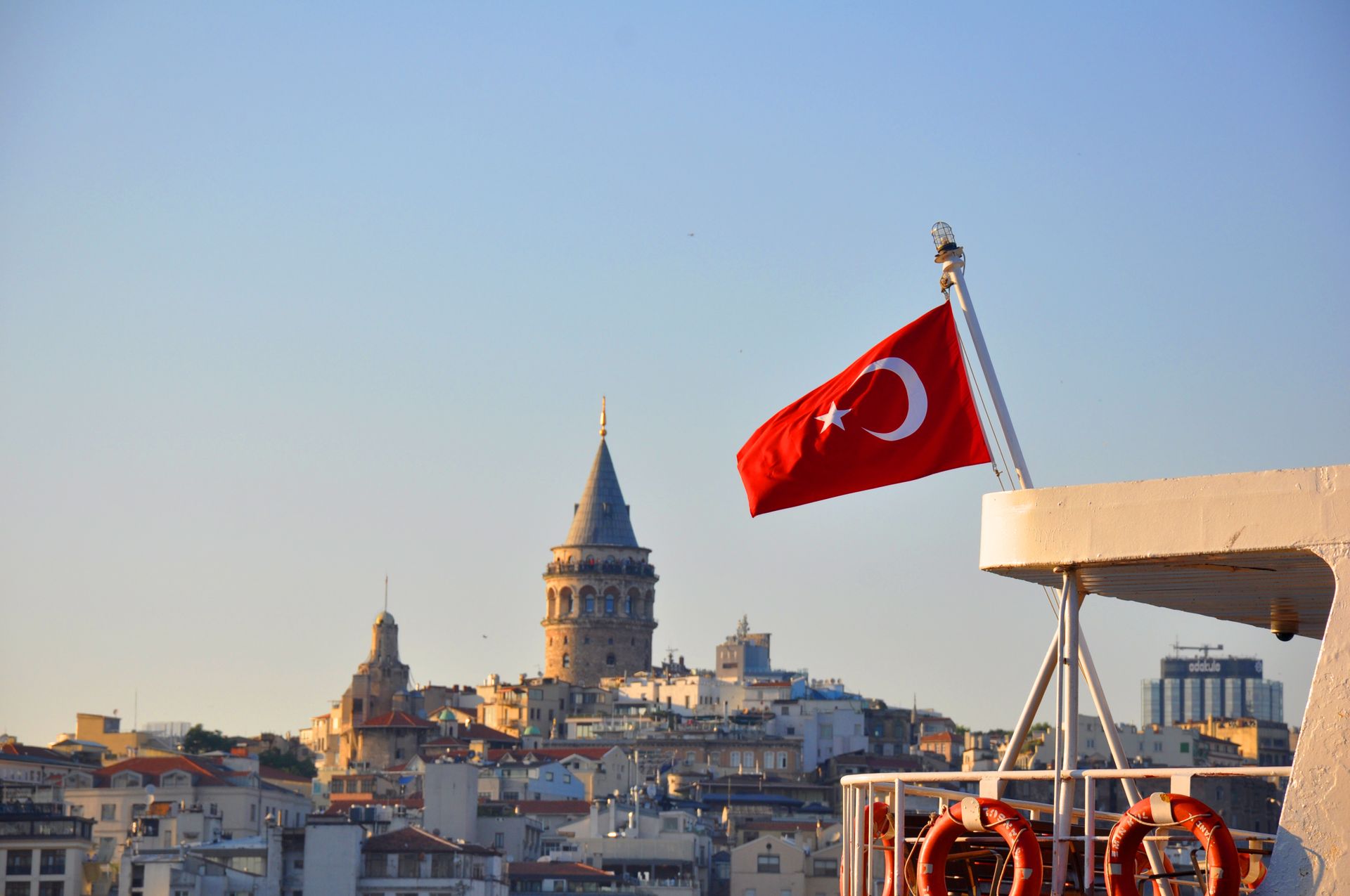 Turkish flag on ferry with iconic Galata Tower in Istanbul's skyline during a sunny day.
