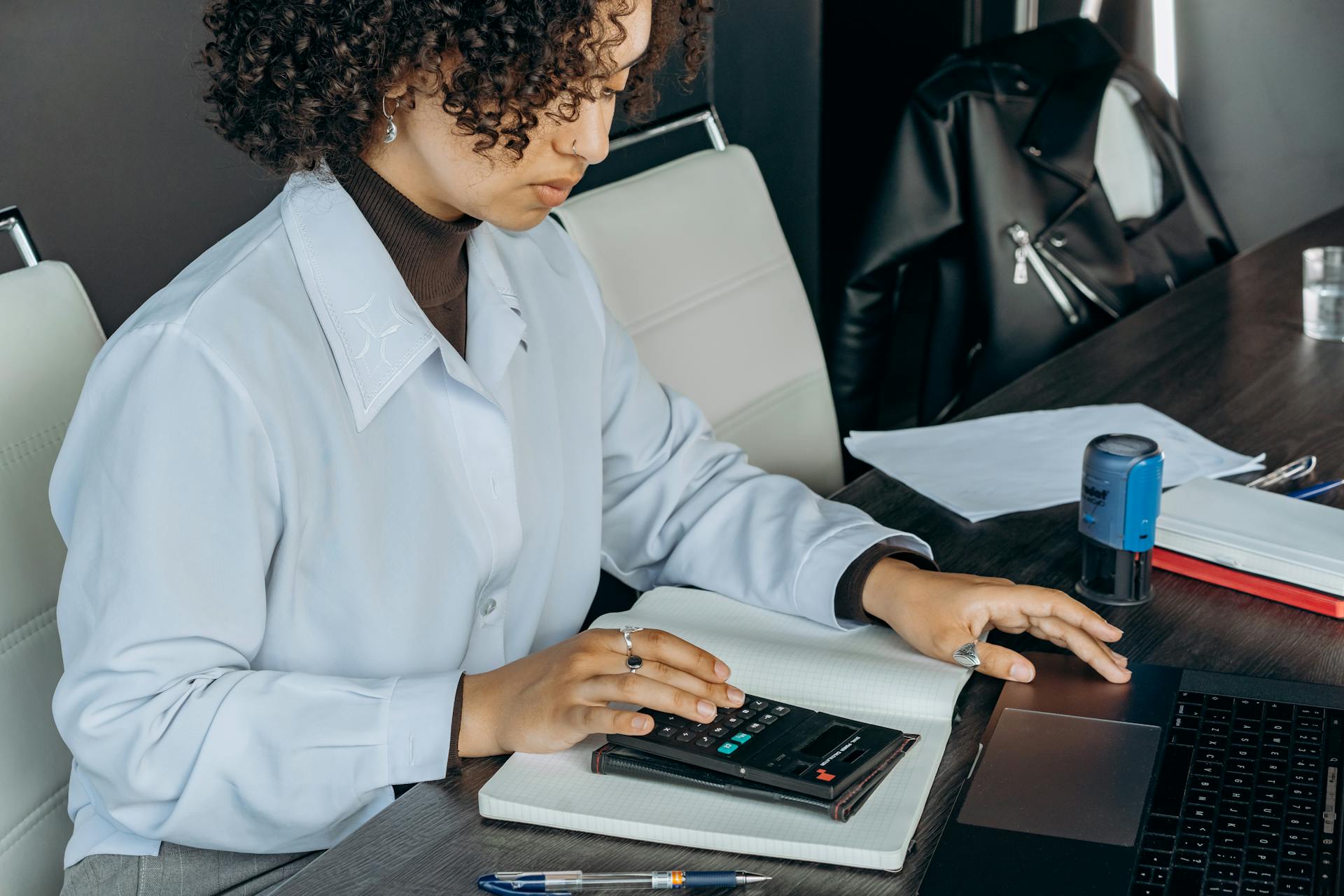 Young woman in office using a calculator for financial calculations.