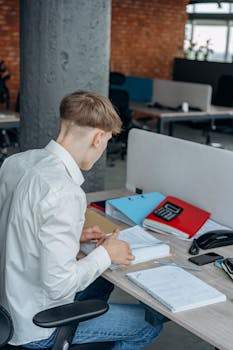 A young professional reviewing documents at a tidy office desk in a modern workspace.