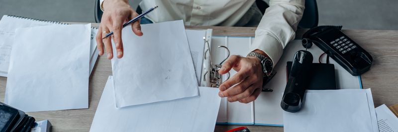 A business professional organizing documents at a busy office desk, emphasizing productivity.