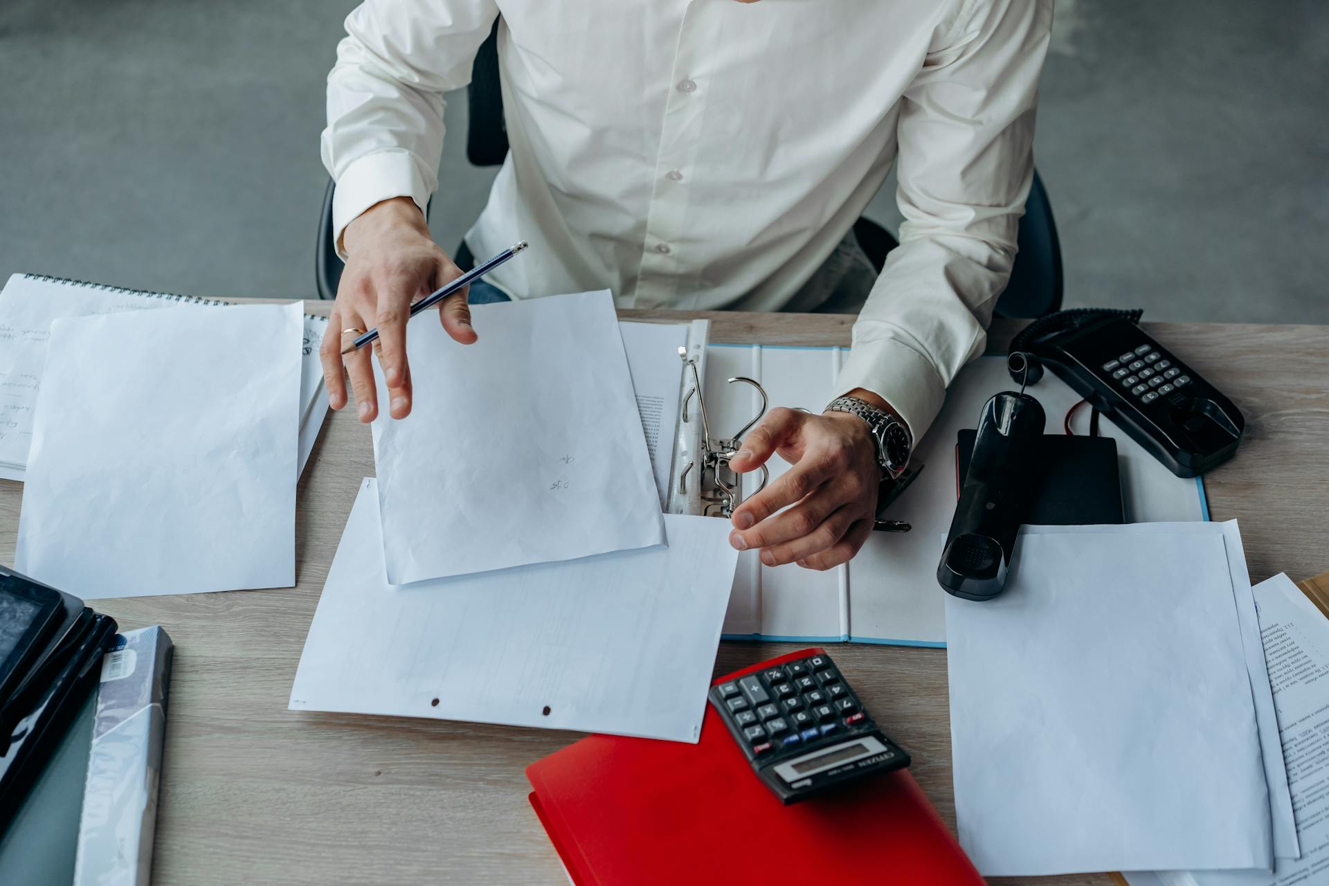 A business professional organizing documents at a busy office desk, emphasizing productivity.