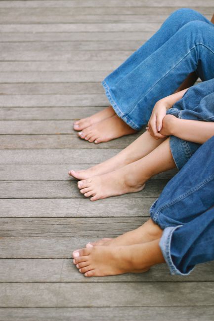 People in denim jeans sitting barefoot on a wooden deck, enjoying a relaxed moment.