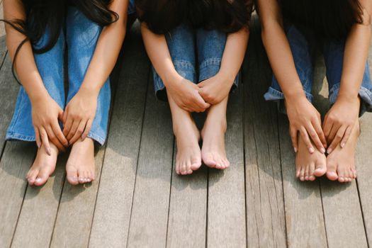 Three friends in denim sitting barefoot on wooden planks outdoors.