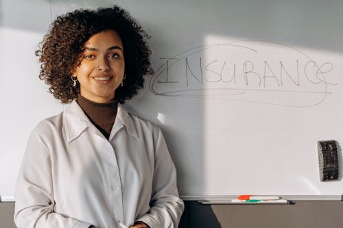 Free A Woman in White Long Sleeves Smiling while Standing Near the Whiteboard Stock Photo