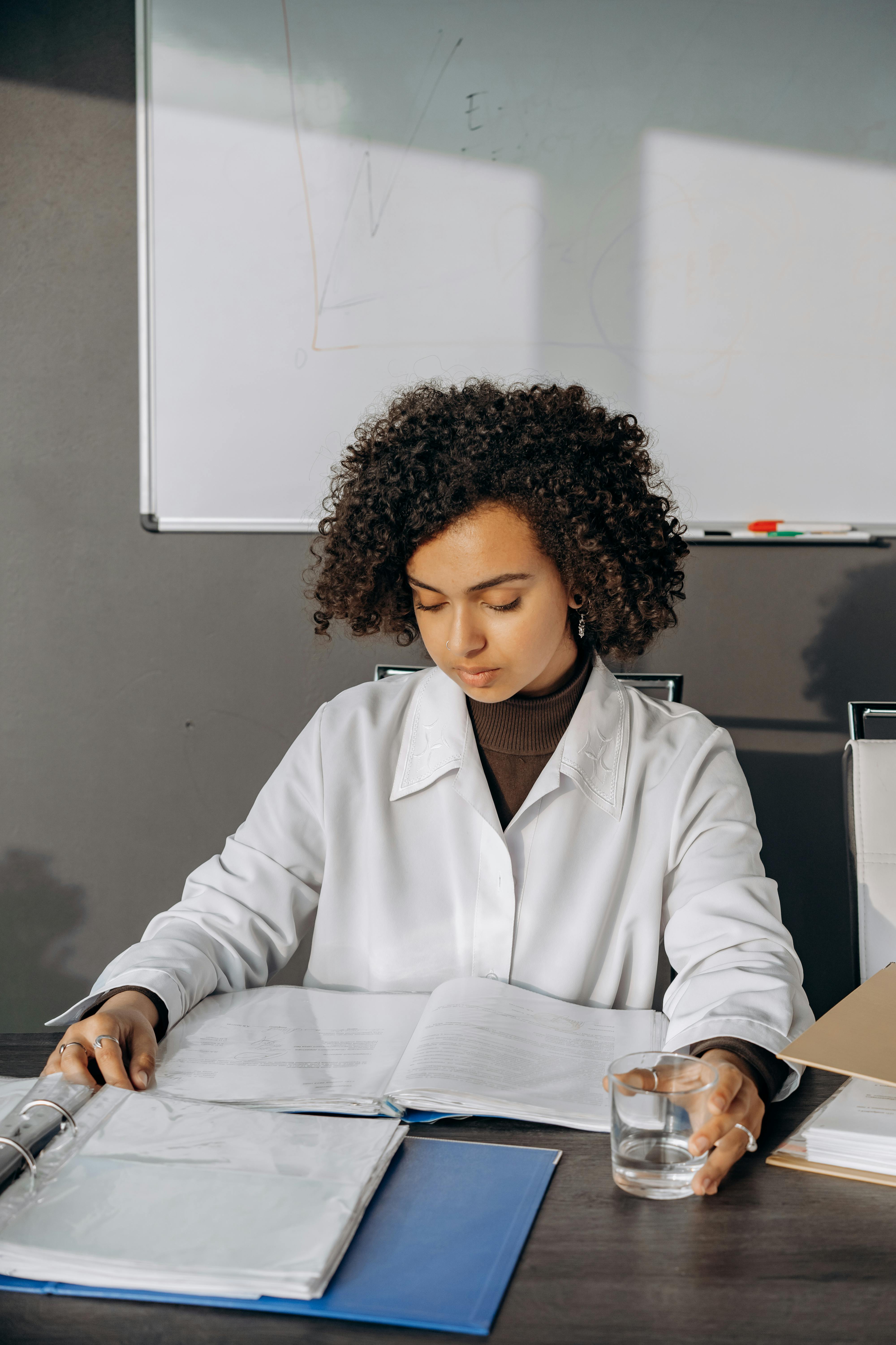 A Woman in White Long Sleeves Working while Holding a Drinking Glass