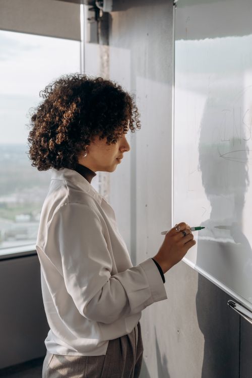 Free Confident woman with curly hair writing on office whiteboard, focused on work. Stock Photo