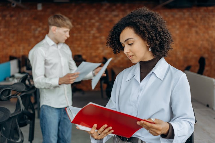 Employees Standing In White Long Sleeve Shirts Holding And Reading Paperwork Inside An Office