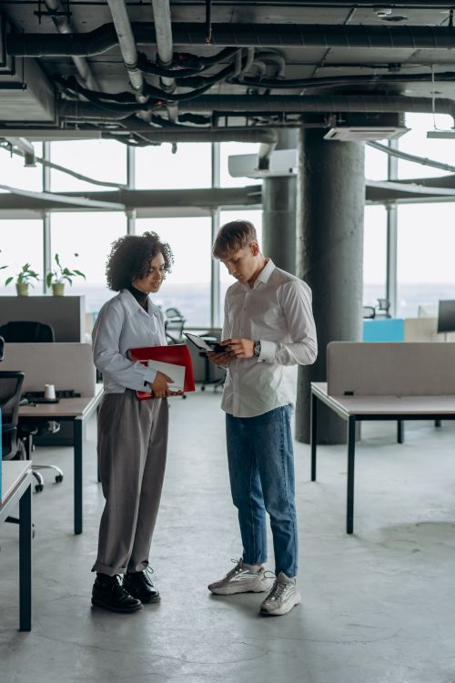 Free Two young professionals engage in discussion amidst a modern office setting, fostering collaboration. Stock Photo