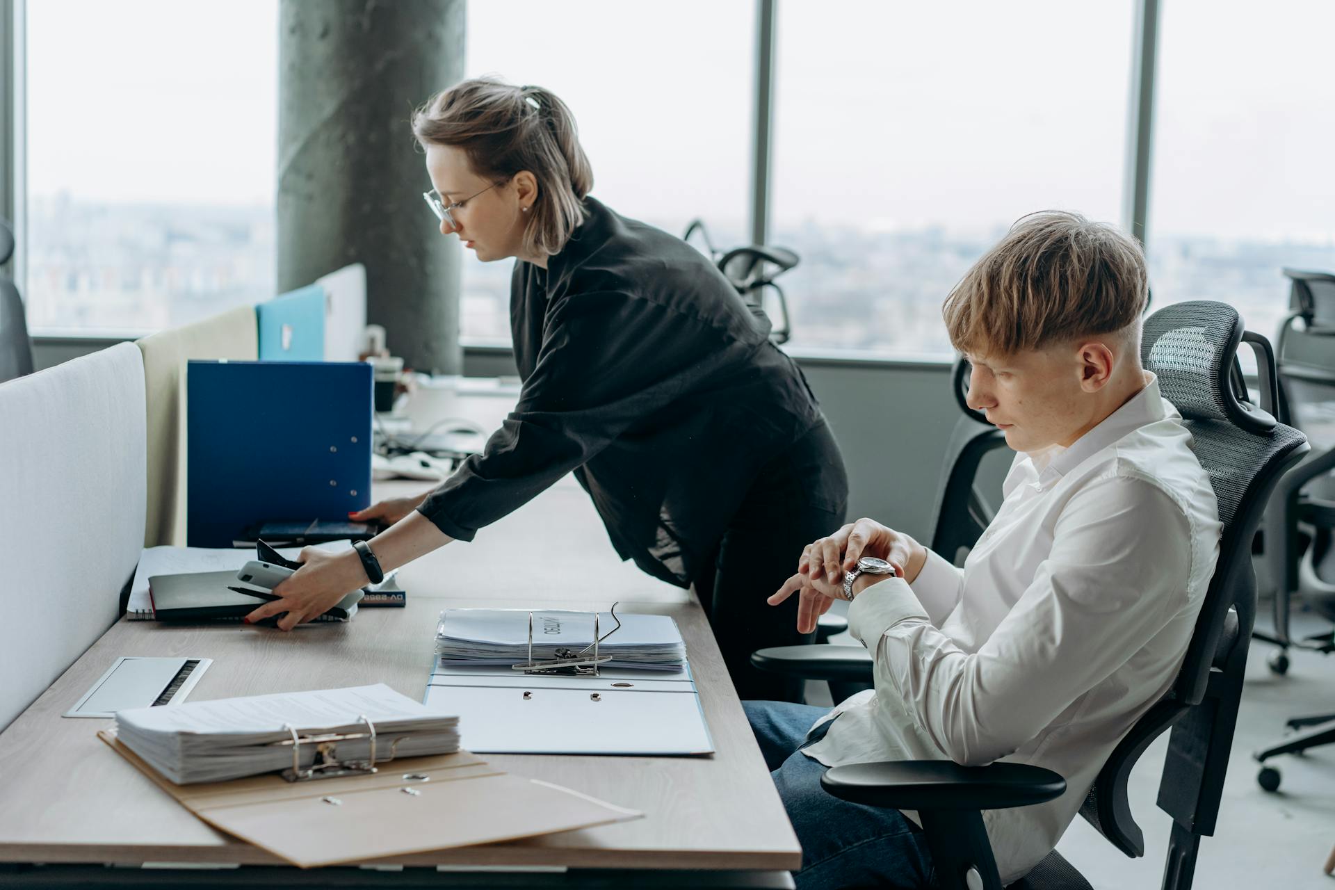 Two business professionals working together in a modern office environment with documents and computers.