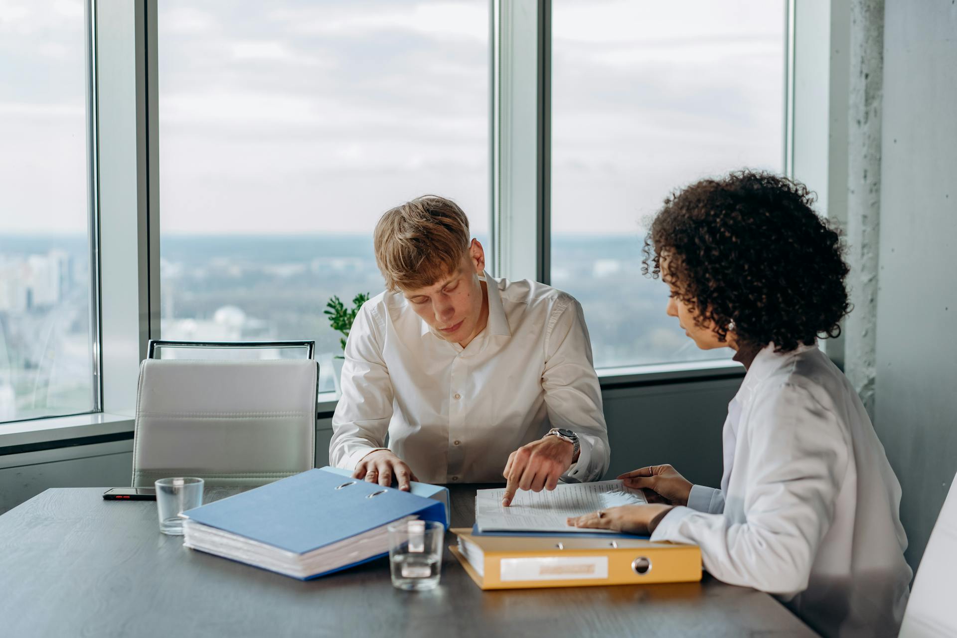 Two professionals reviewing documents in a high-rise office with city views.