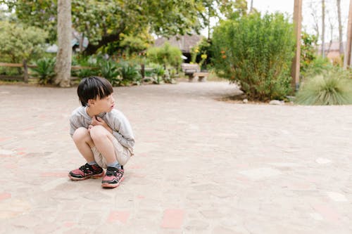 A Boy Sitting on the Ground Near Green Plants while Looking Afar