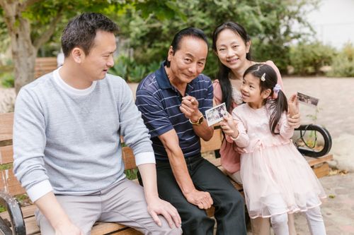 Free A joyful multigenerational family enjoying time together on a park bench, holding photographs. Stock Photo