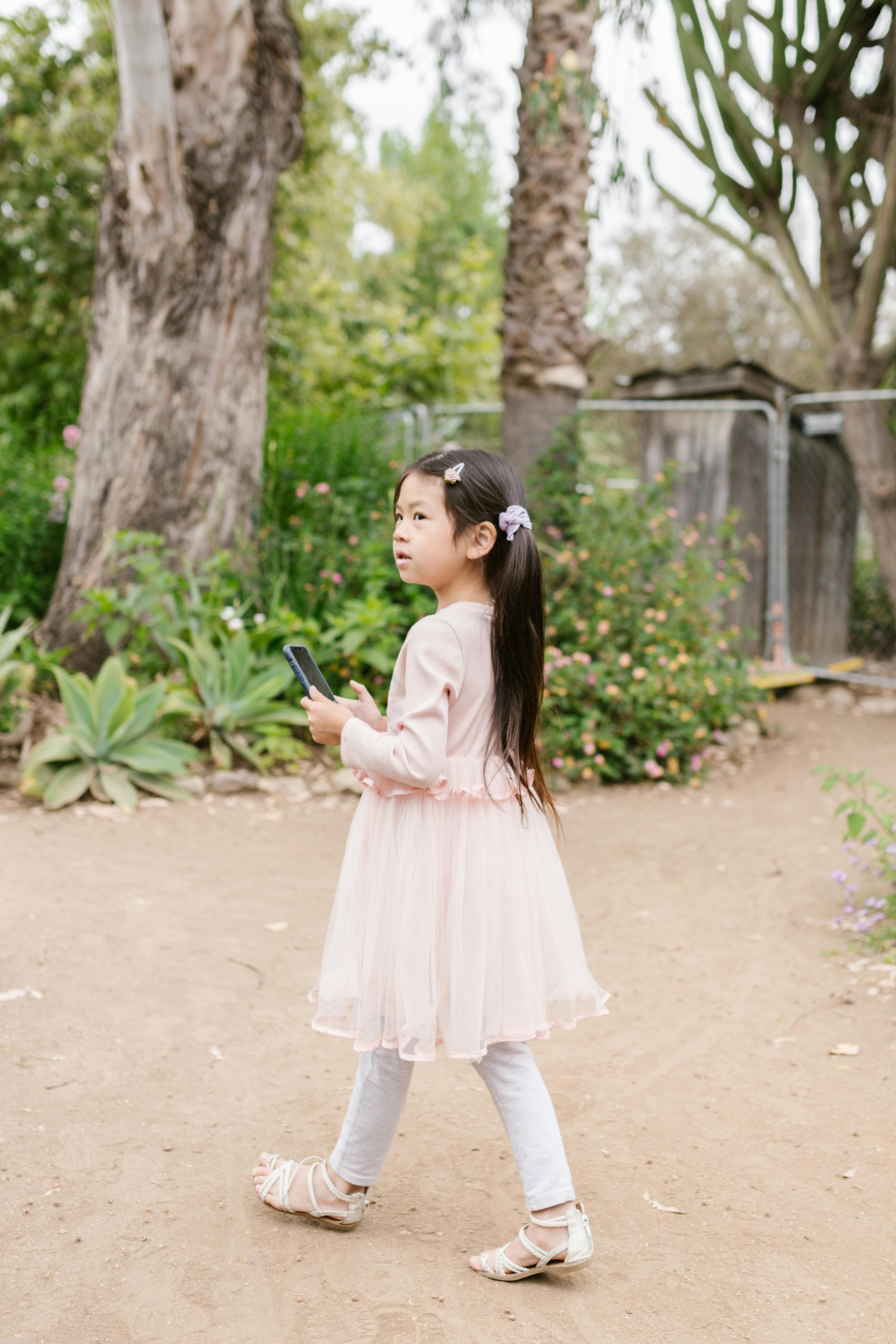 girl in pink dress holding black smartphone