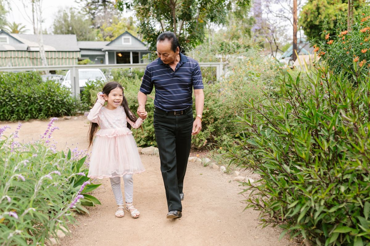 Grandfather walking hand in hand with his young granddaughter along a garden path