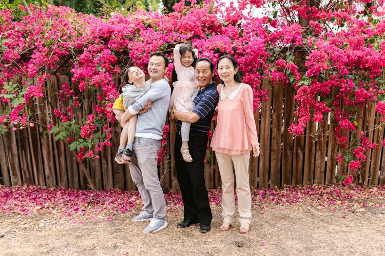 A Happy Family Standing Near The Bougainvilleas