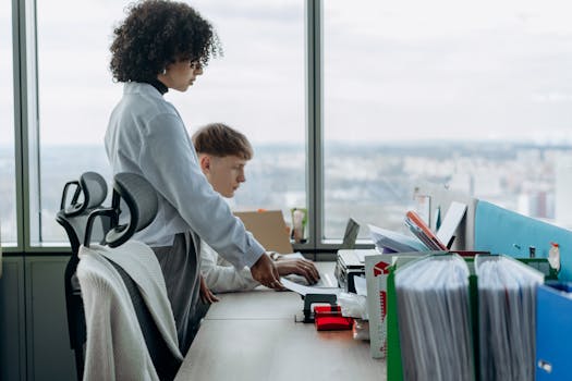 Two coworkers collaborate in a modern office with a city view, enhancing teamwork and productivity.