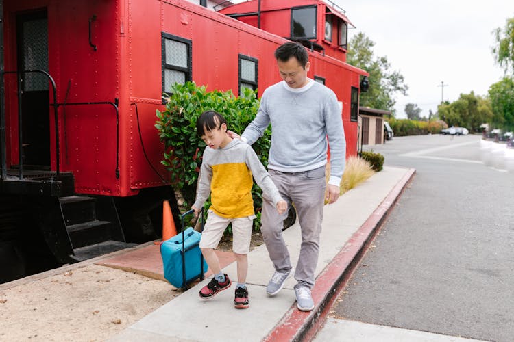 Father And Son Walking On Concrete Sidewalk Near A Red Train