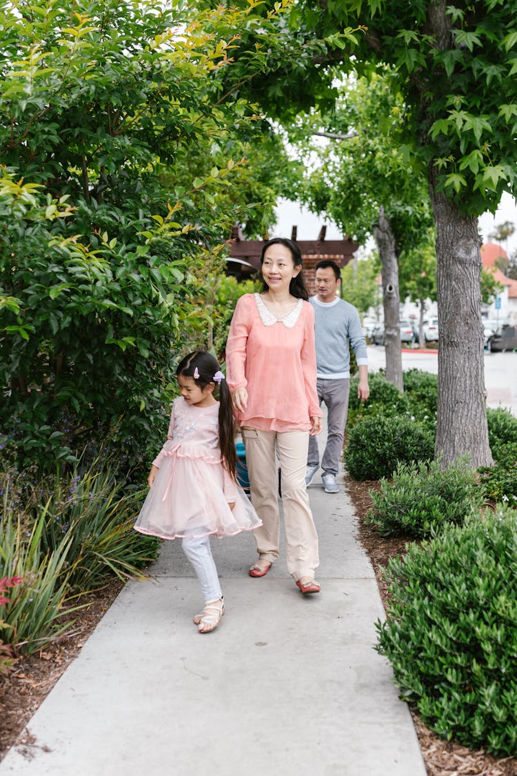 A Child Holding A Woman's Hand Walking Together On A Sidewalk