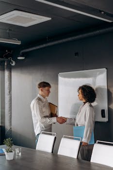 Two professionals shaking hands in a modern office setting.